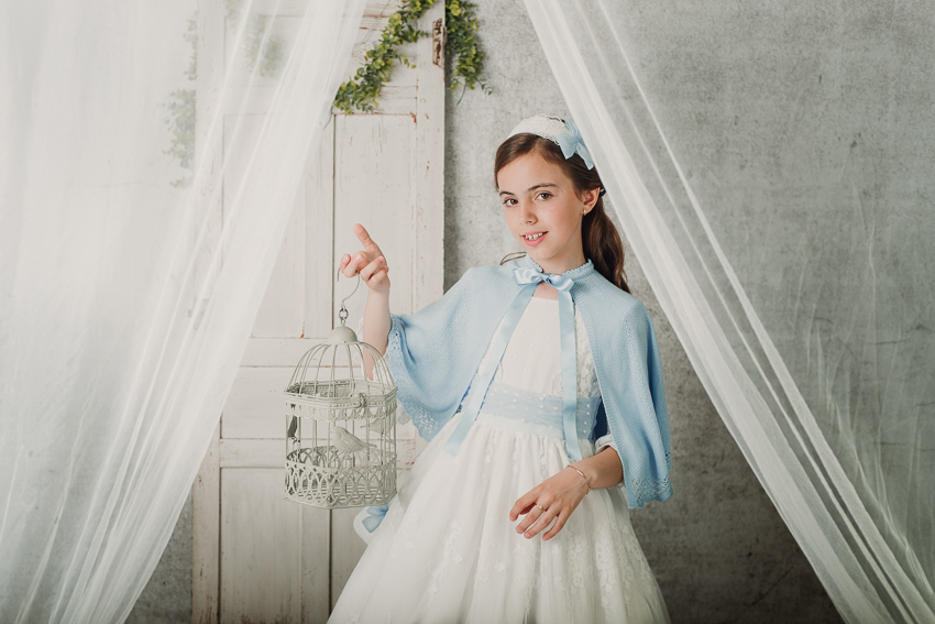retrato de niña de comunión en estudio sujetando una jaula con la mano