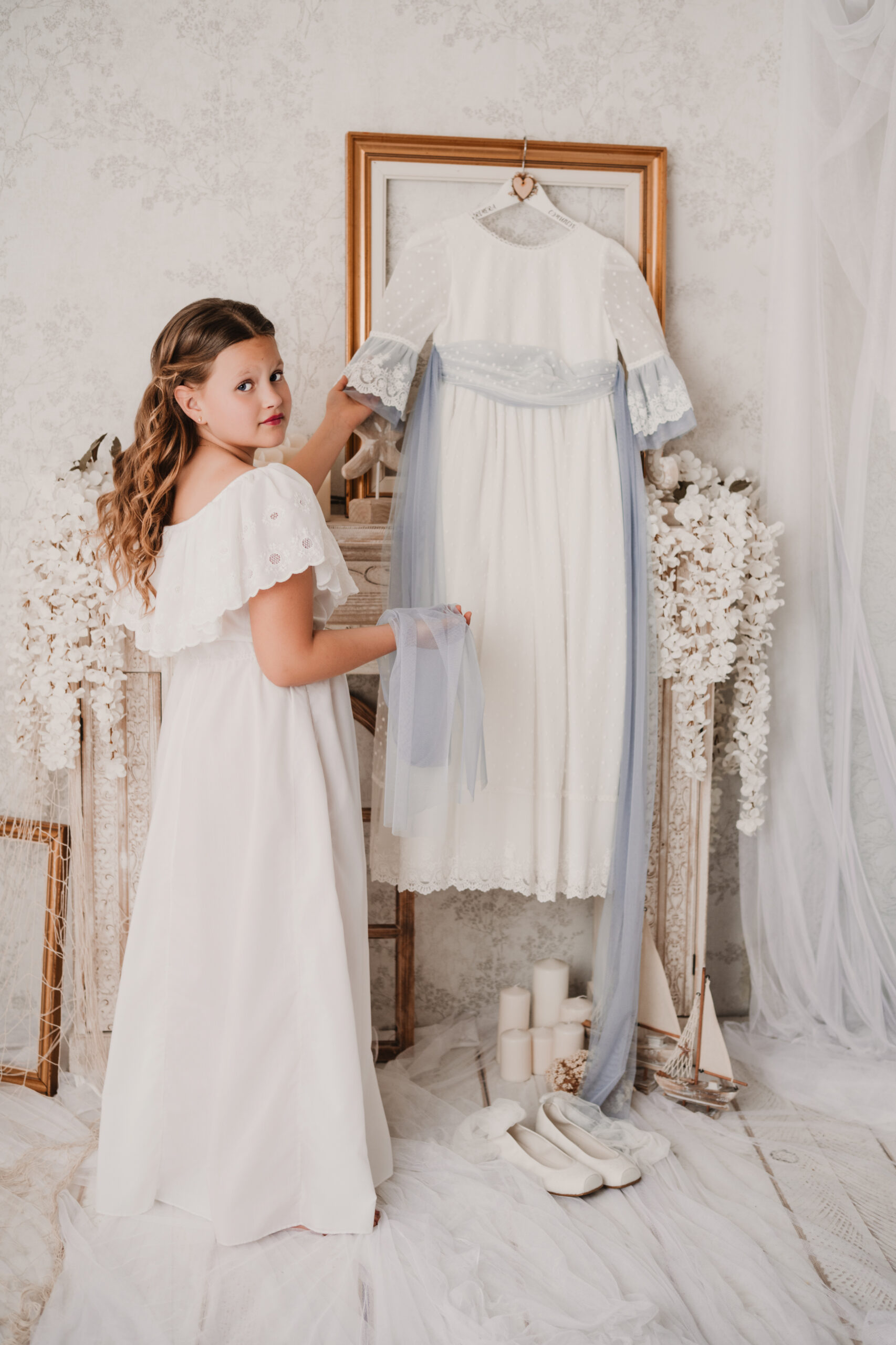 Detalle del traje y Niña con camisón sosteniendo su vestido de comunión durante una sesión de fotos en Jaén